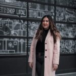 Georgia standing in front of windows with white drawings on them in a pink coat