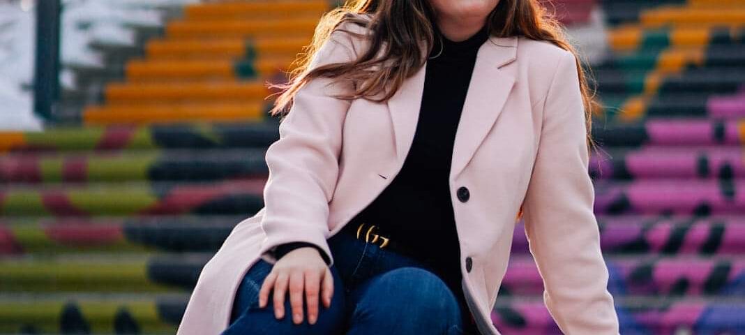 Georgia is sitting on an outdoor painted staircase in a pink coat